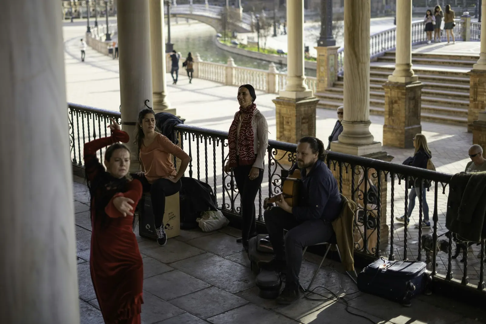 A dancer in a red dress, a seated singer in a red scarf and a guitarist perform together under the arcades of Plaza de España in Seville